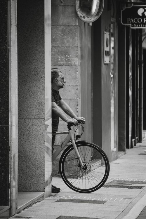 Free Black and white photo of an elderly cyclist resting in Valencia, Spain's cityscape. Stock Photo