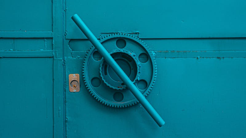 Close-up of a teal metal door with industrial gear mechanism, showcasing intricate machinery details.
