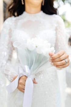Close-up of a bride holding a beautiful white tulip bouquet in a delicate lace wedding dress.