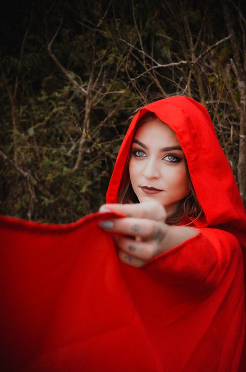 Free Portrait of a woman in a red hood, exuding mystery and allure in a forest setting. Stock Photo