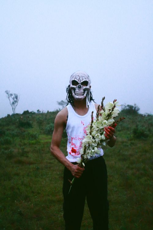 Free A masked figure in a tank top holding flowers on a misty day, evoking a spooky Halloween vibe. Stock Photo
