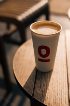 Disposable coffee cup with foam on a wooden table outdoors, sunlit in Istanbul.