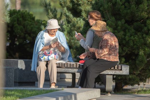 Elderly women enjoy a sunny day playing cards on a bench in a park setting, capturing leisure and friendship.