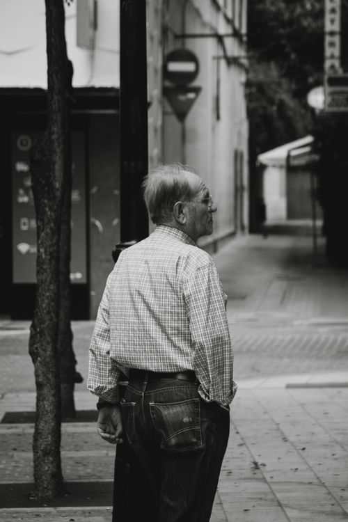 Free Black and white portrait of a senior man walking in a quiet city alleyway. Stock Photo