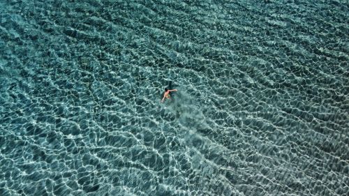 Free Relaxing aerial shot of a woman swimming in crystal-clear Greek waters, capturing summer tranquility. Stock Photo