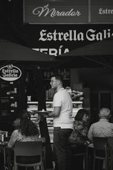 A black and white capture of a waiter serving guests in an outdoor restaurant setting.