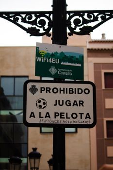 Spanish sign forbidding ball games with humorous graffiti in city street.