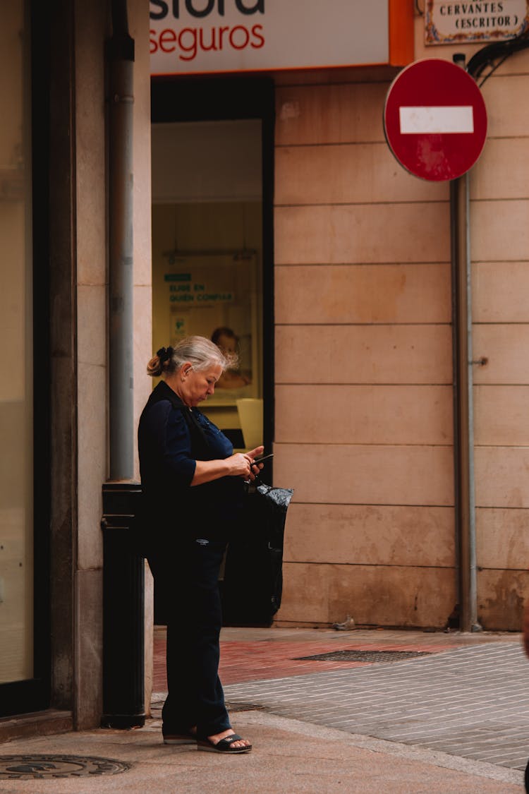 Elderly Woman Checking Phone On Sidewalk