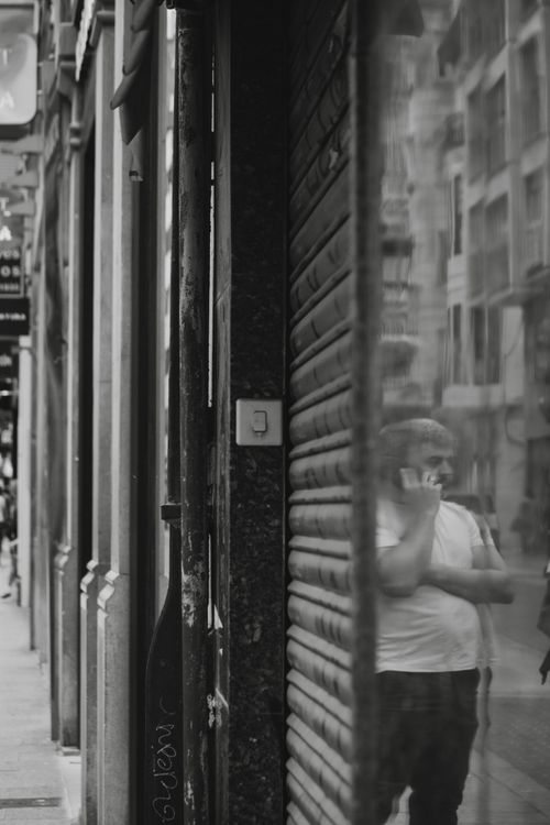 Free A black and white street scene featuring a man's reflection while talking on the phone. Stock Photo