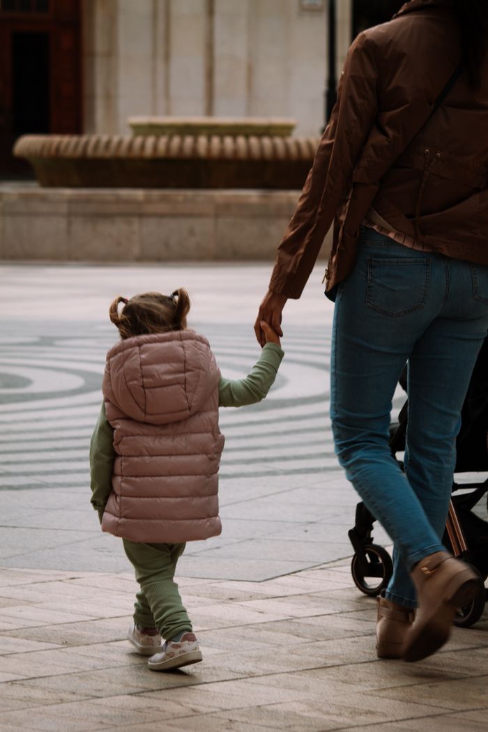 A mother and daughter holding hands, seen from behind, walking down a street