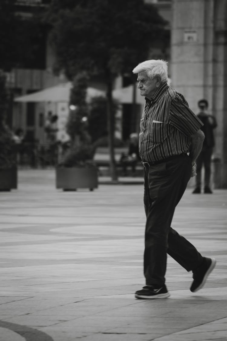 Black And White Photo Of A Senior Gray Haired Man Walking On A Street