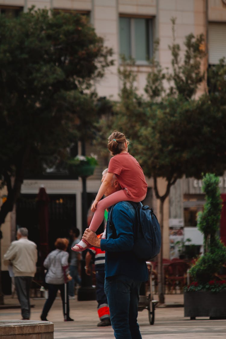 Man Carrying Daughter On His Shoulders On A Street