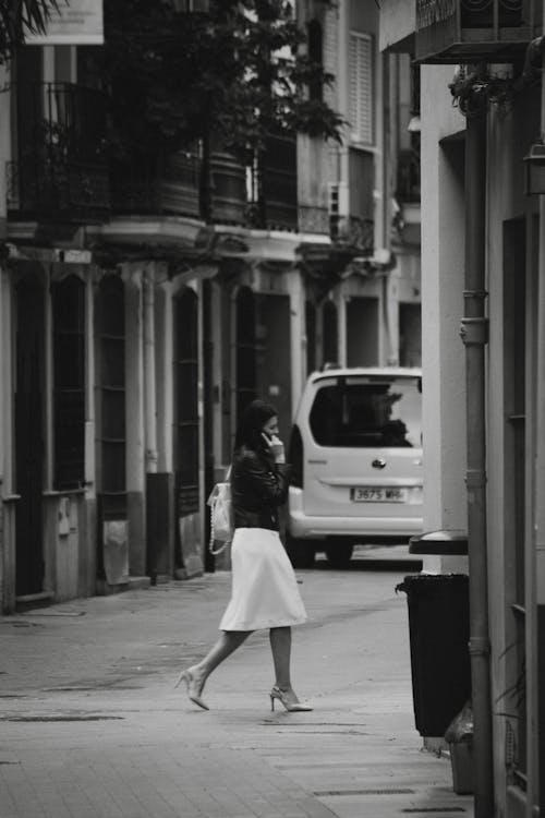 Woman in White Skirt and Black Leather Jacket Crossing a Street
