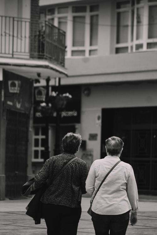 Free Two elderly women stroll down a city street in a monochrome setting, showcasing urban life. Stock Photo