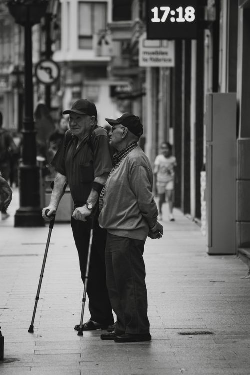 Free Black and white photo of two elderly men conversing on a city street. Stock Photo