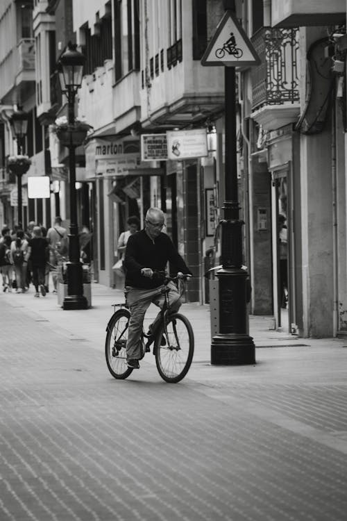 Black and White Photo of a Senior Man Riding on a Bicycle on a Street