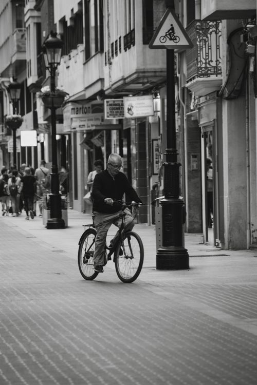Free Black and white photo of a senior man cycling through a city street. Stock Photo