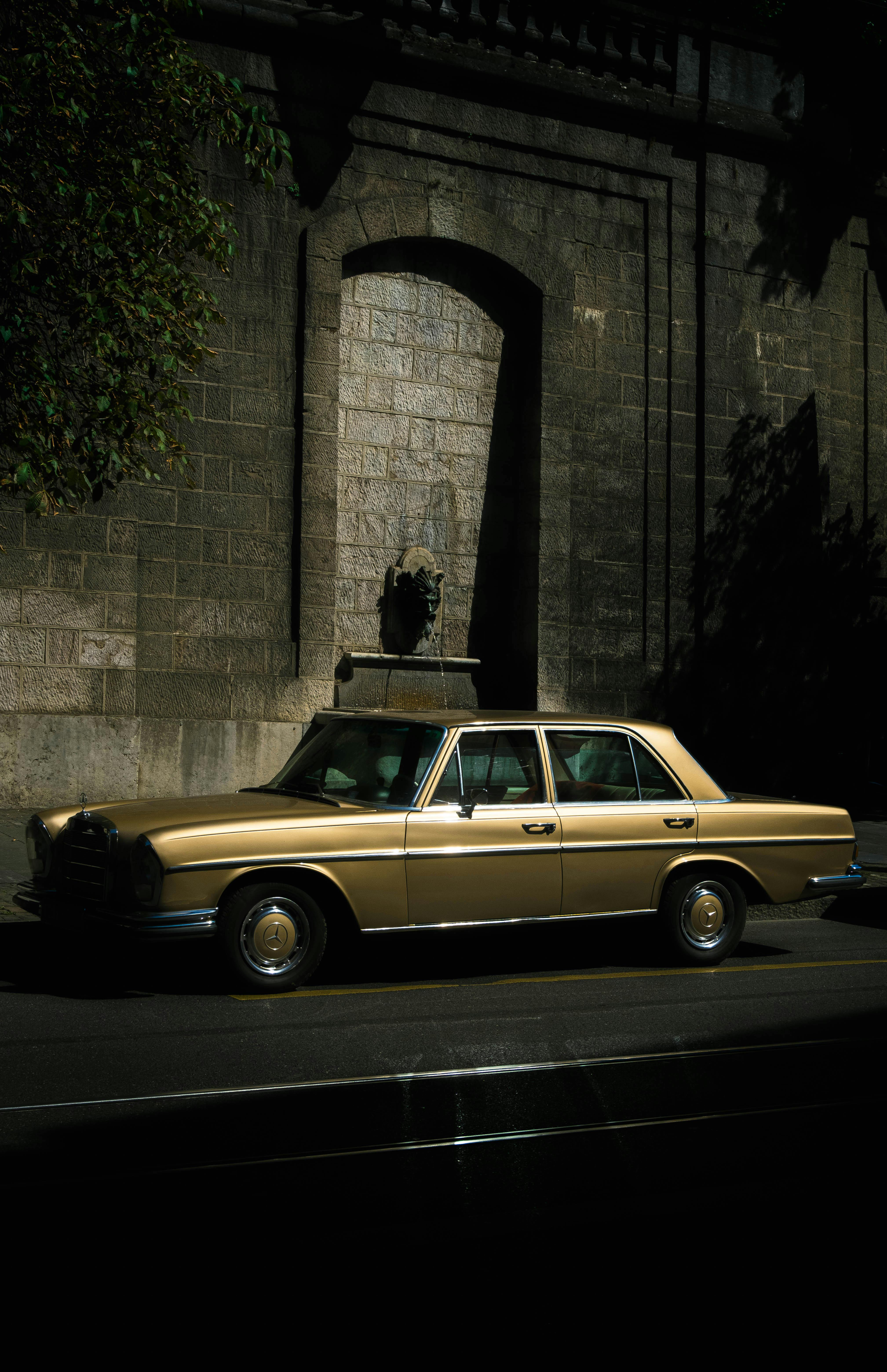 Classic vintage car parked on a sunny city street under an arched stone structure.