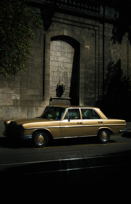 Classic vintage car parked on a sunny city street under an arched stone structure.
