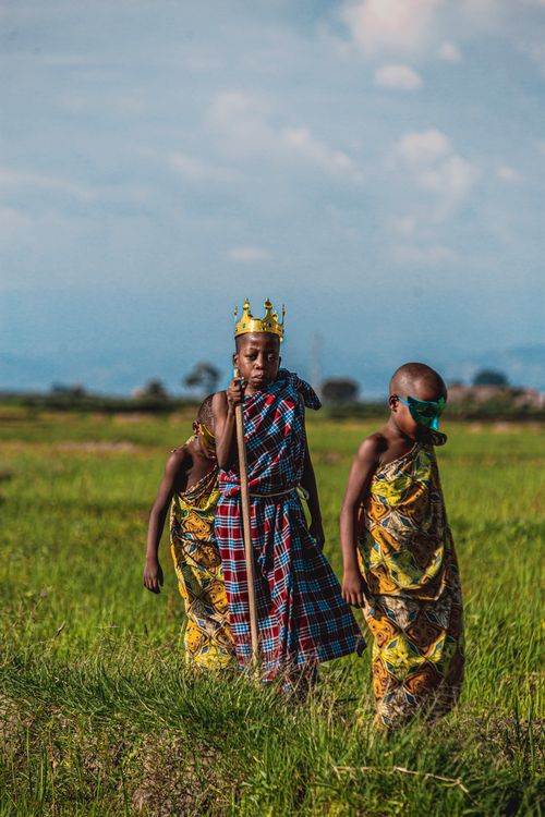 Free Three children in vibrant traditional attire play in a green field under a summer sky. Stock Photo