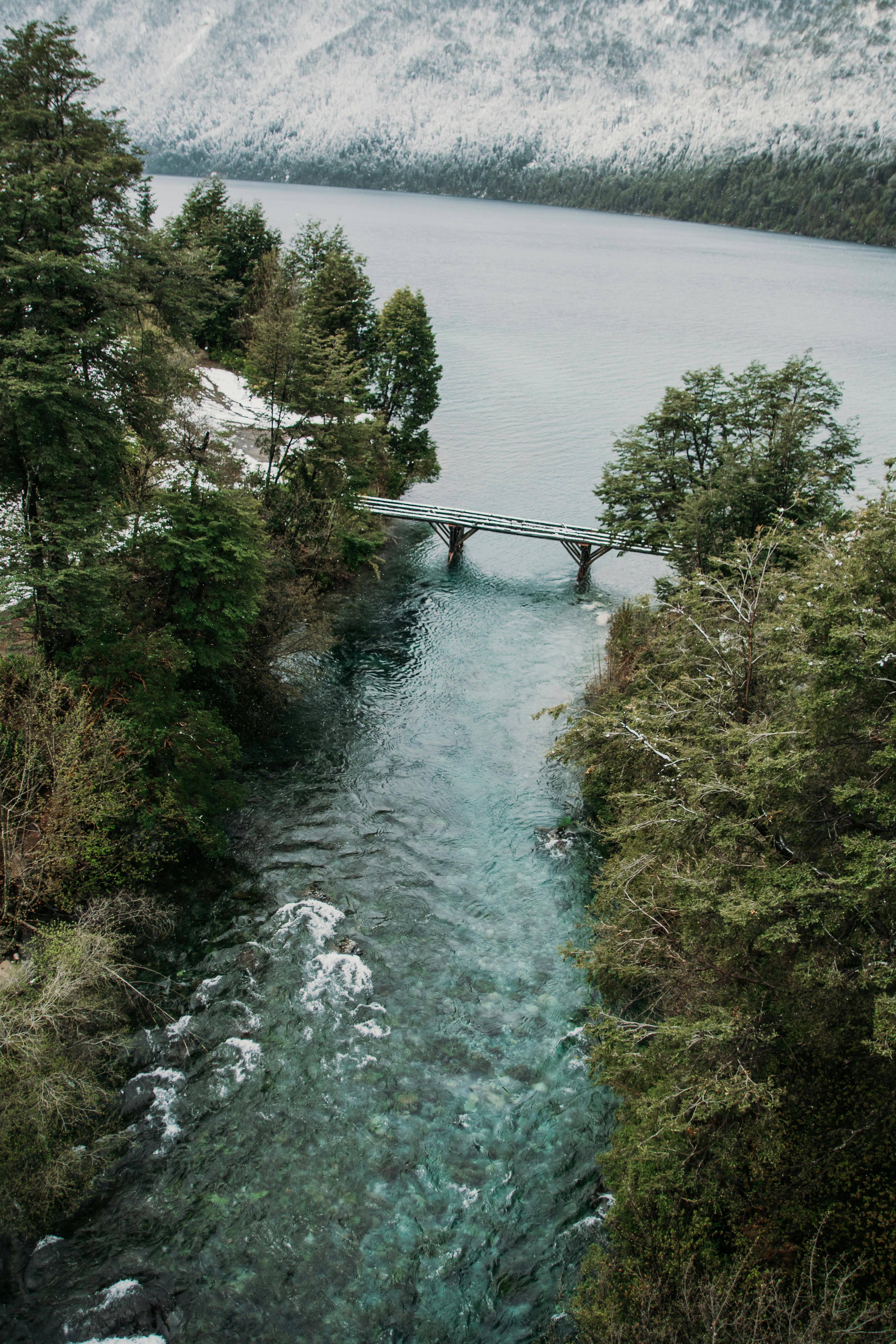 Stunning aerial shot of a bridge spanning a turquoise river surrounded by lush forest and mountains.