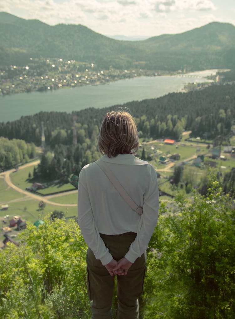 Back View Of A Woman Standing On A Hill And Looking At A River In The Valley 