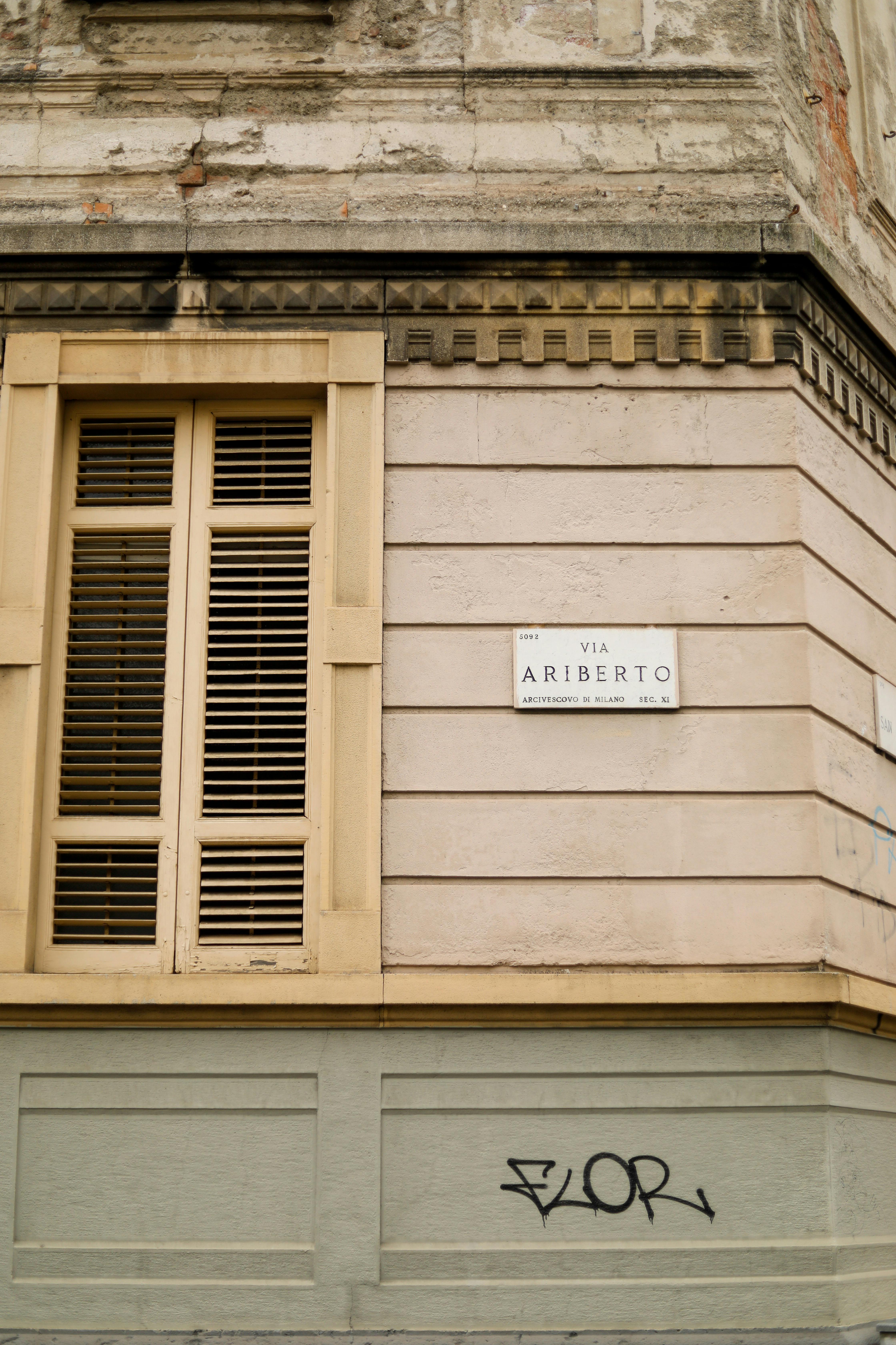 Free Close-up of a historic urban building facade featuring a window with shutters and graffiti on the wall. Stock Photo