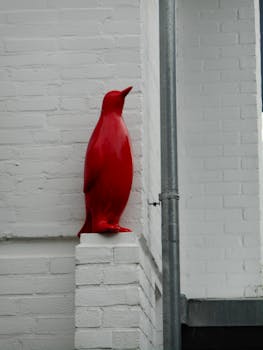 A striking red penguin figurine decorates a white brick wall corner.