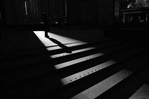 Free A solitary silhouette of a pedestrian casting a long shadow on urban street steps in a cityscape. Stock Photo