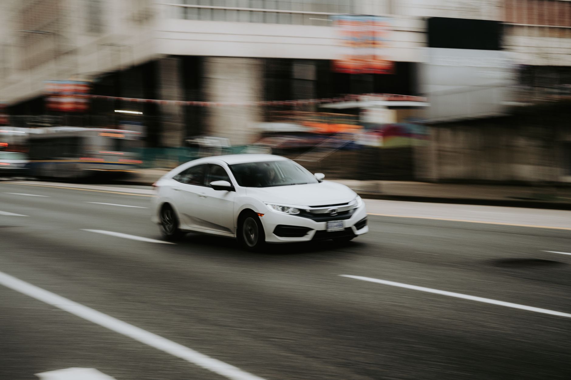 A white car speeding through an urban street, highlighting motion and city life.
