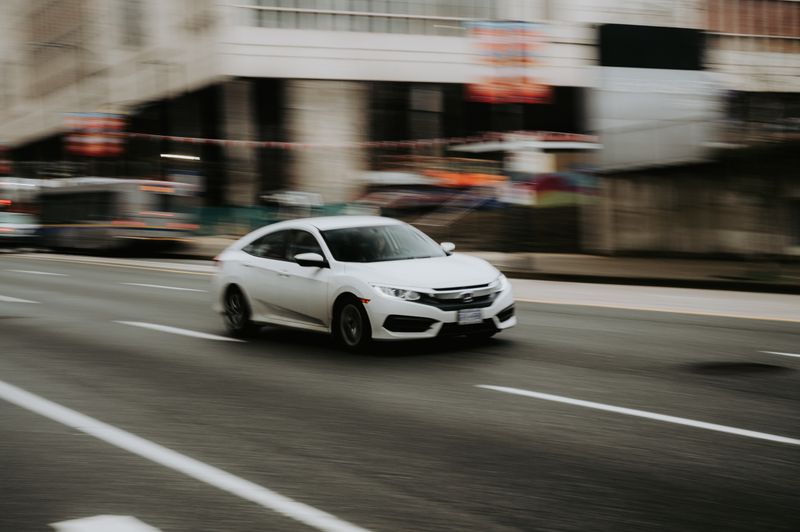 A white car speeding through an urban street, highlighting motion and city life.