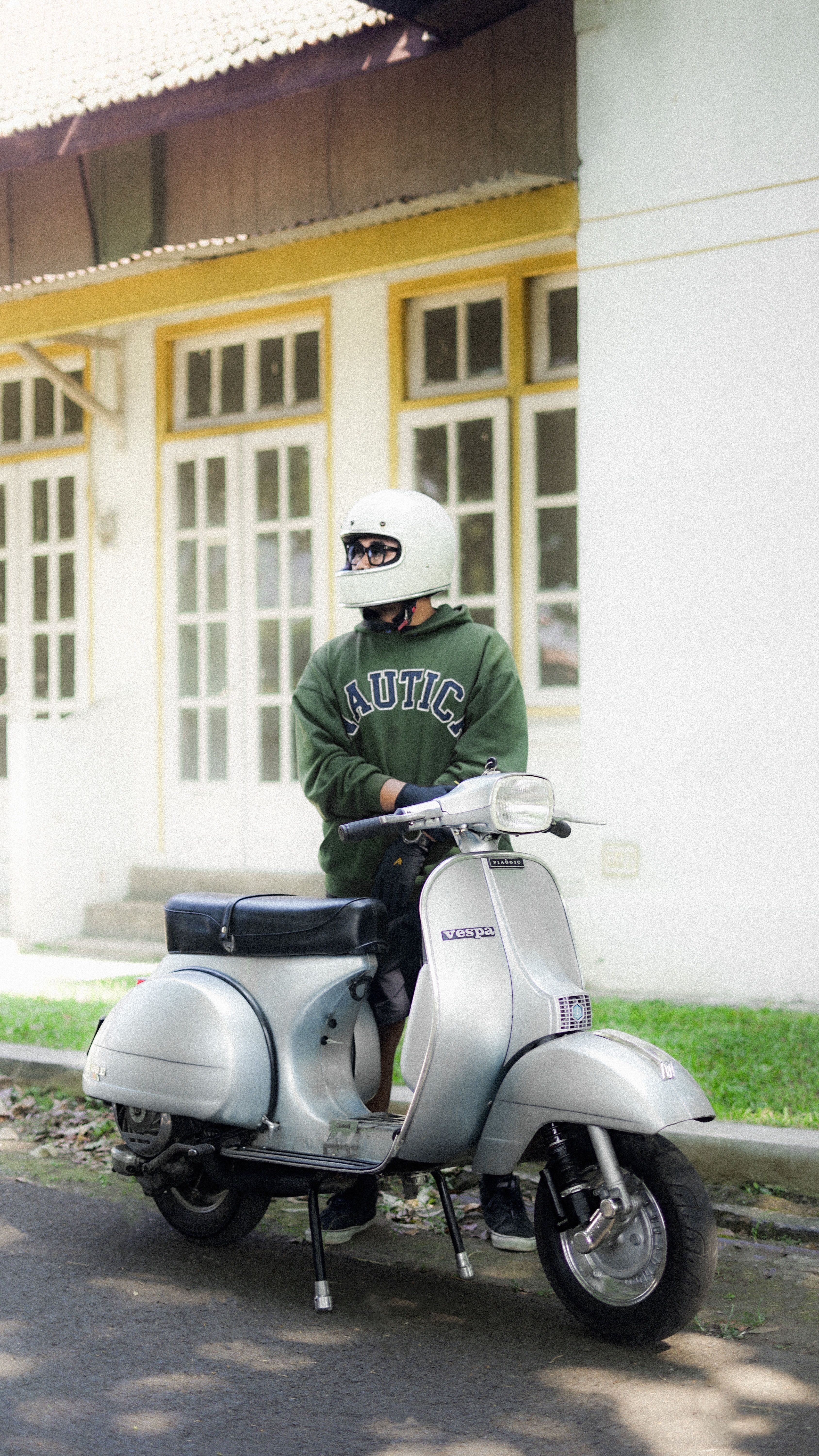 Casually dressed man with helmet sits on a vintage scooter outside a building.