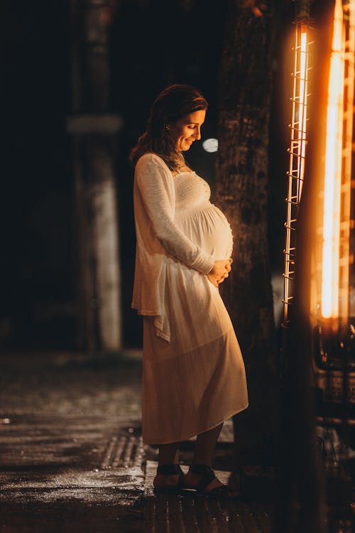 Pregnant Woman in a Dress Holding Her Stomach and Smiling 
