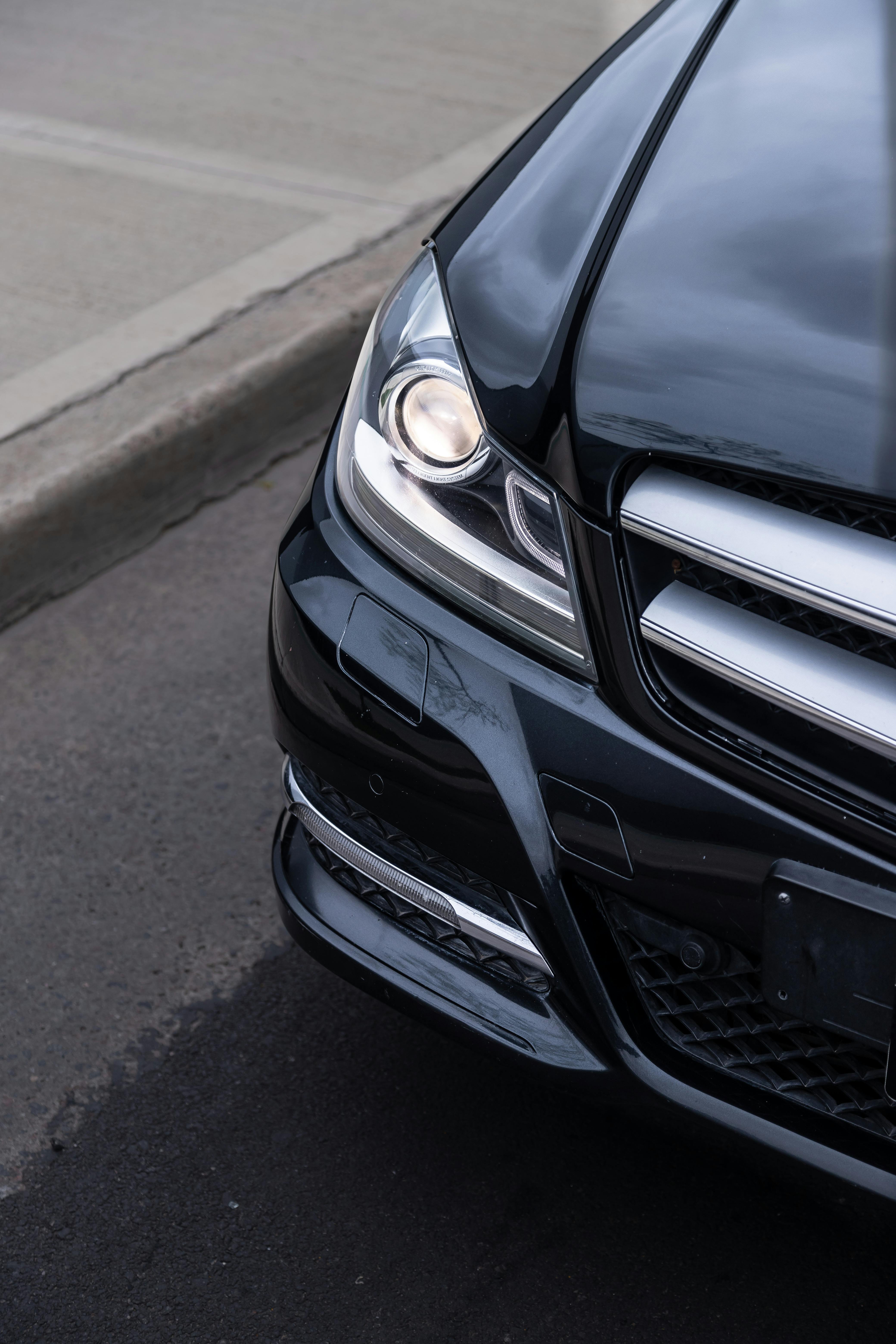 Free Elegant close-up of a shiny black car with headlights on a city street. Stock Photo
