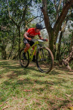 A determined cycler tackles an uphill trail in a green forest under the summer sun.