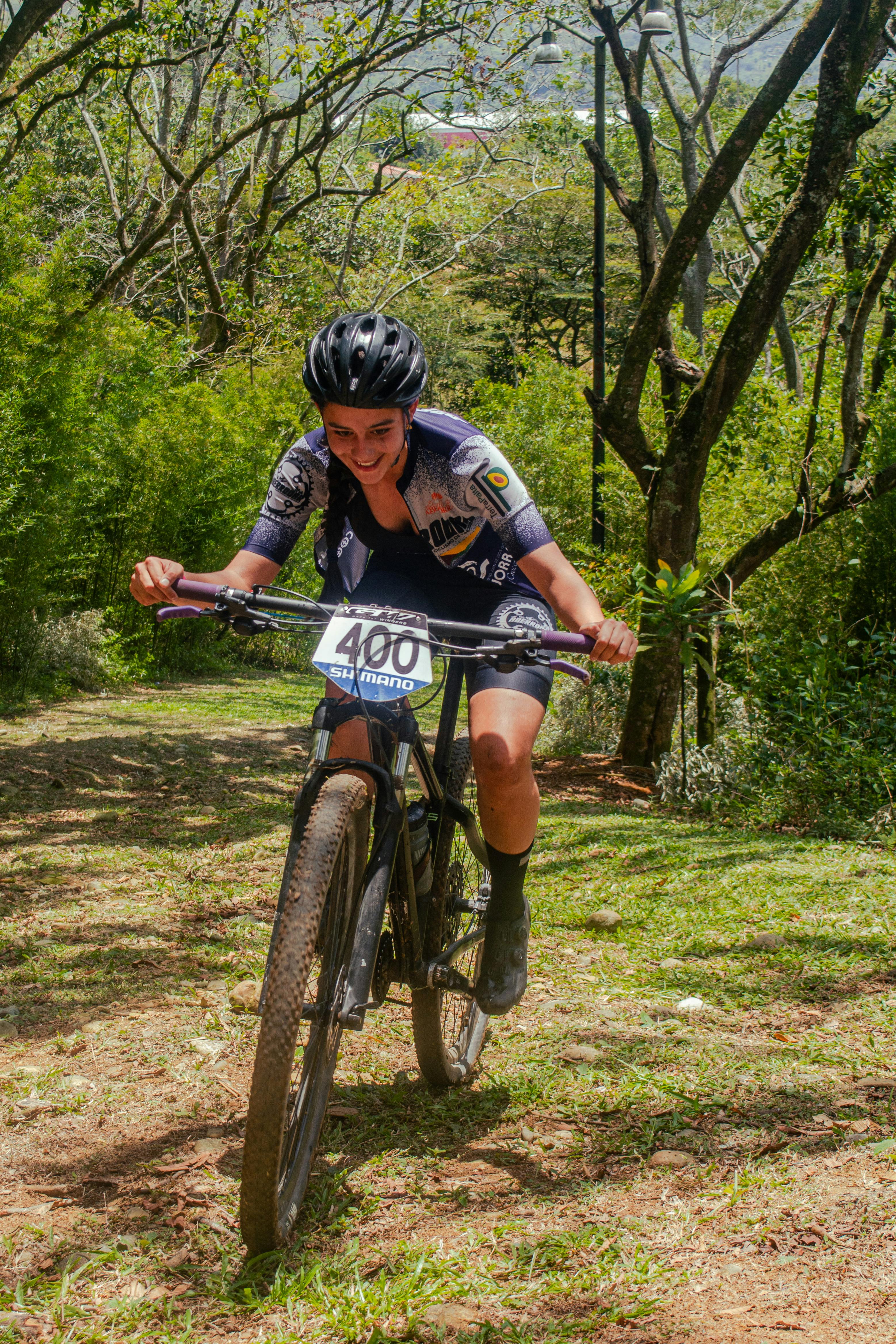 Teenage girl cycling in a race through a scenic forest trail, smiling and enjoying the sport.