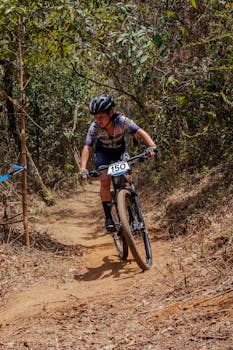 Teenager racing on a mountain bike through a forest trail, illustrating athleticism.