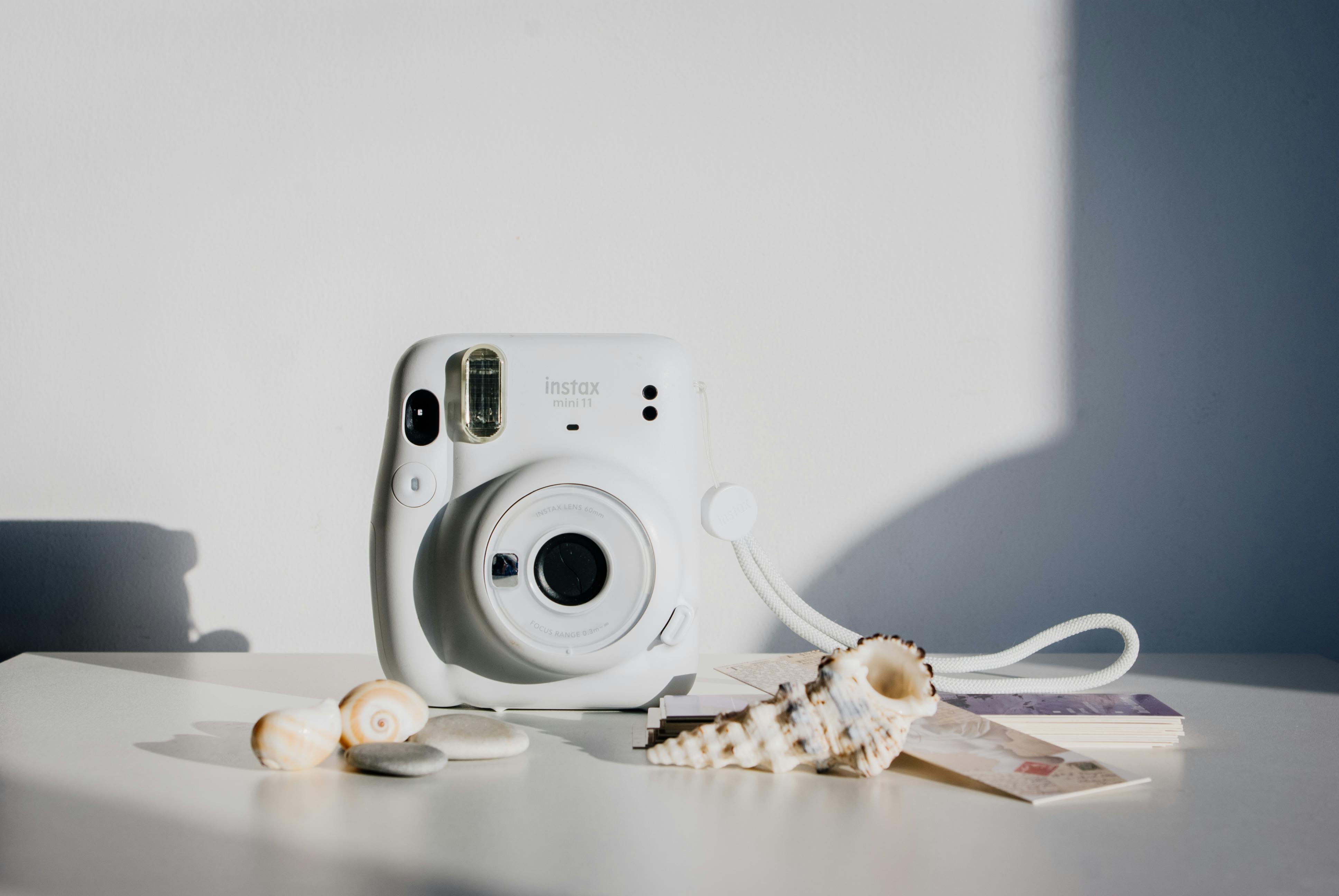 White instant camera placed on a table with seashells and a postcard. Minimalist and artistic composition.