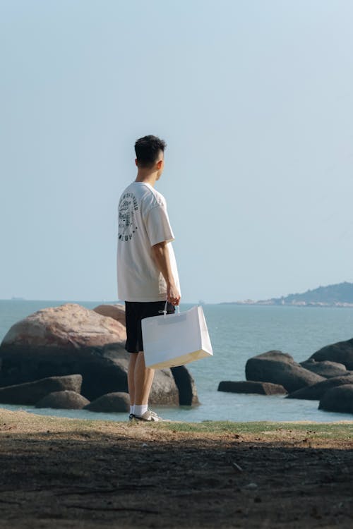 A Man Holding a Paper Bag Standing on the Shore 