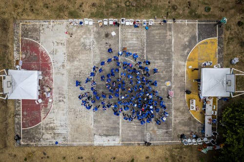 Drone Shot of People in Blue Clothes Gathered on an Old Basketball Court Outside 