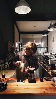 A barista pours coffee in a cozy modern café setting with warm lighting.