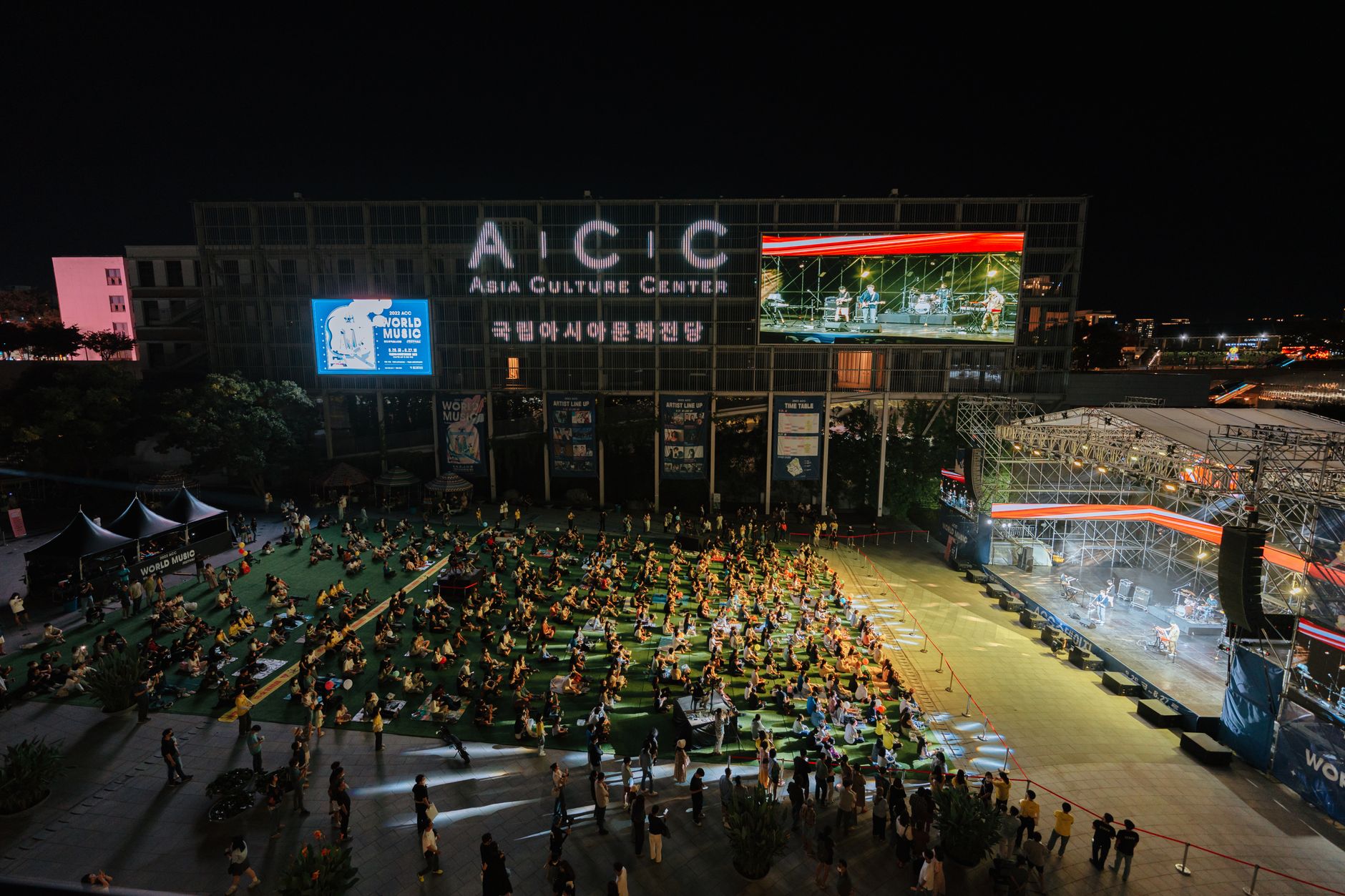 A vibrant outdoor concert at the Asia Culture Center, bustling with a lively crowd at night.