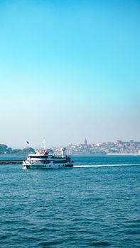 Peaceful scene of a yacht sailing near the coastline with a city backdrop under clear skies.