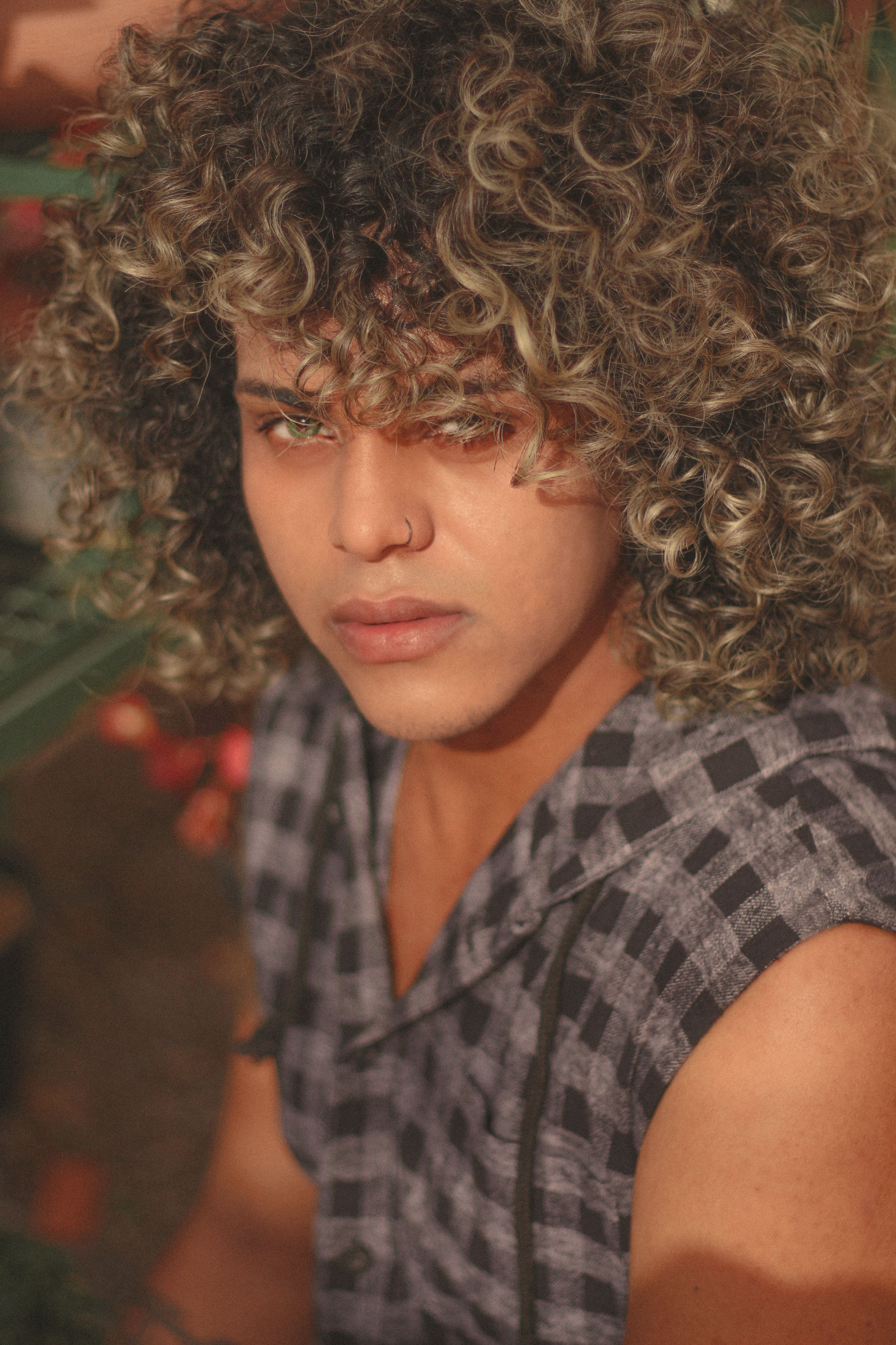 Close-up of a young adult with curly hair wearing a checkered shirt, exuding individuality and style.