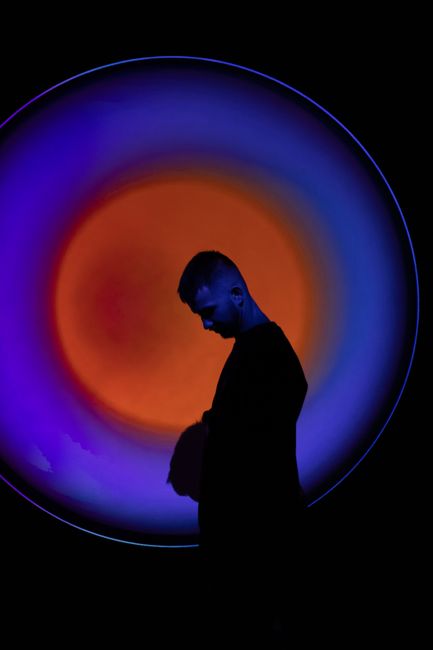 Silhouette of a man against a vibrant orange and blue circular abstract light display.