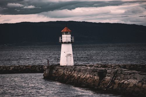 Free A solitary lighthouse on a stormy Norwegian coast, perfect for maritime themes. Stock Photo
