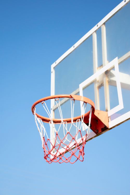Free Close-up of a basketball hoop with a net on a clear blue sky background, perfect for sports themes. Stock Photo