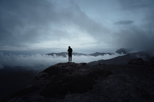 Silhouette of a Man Standing on a Rocky Mountain Peak above Clouds