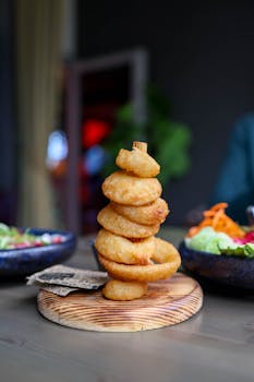 Crispy fried onion rings stacked elegantly, served with salads in a modern restaurant.