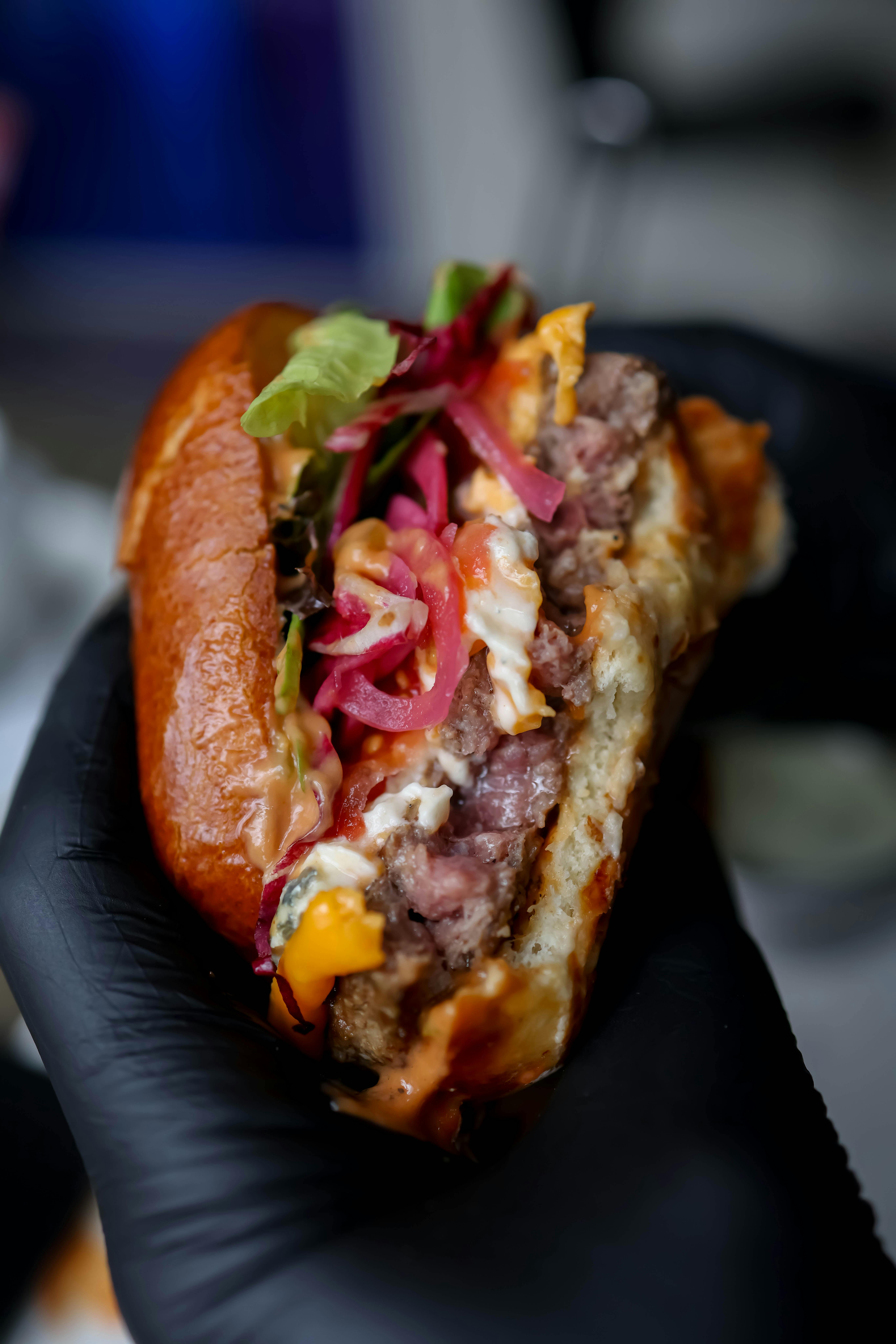 A lamb burger on a brioche bun topped with fresh herbs and preserved lemon, with coral-colored harissa mayo visible on the sides